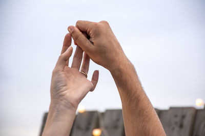 Close-up of hand holding hands against sky