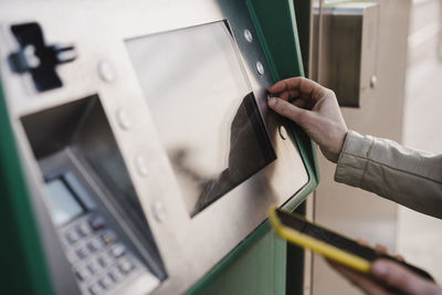 Woman operating ticket machine while holding smart phone