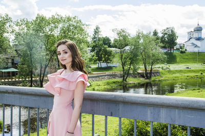 Portrait of beautiful woman standing by railing at park