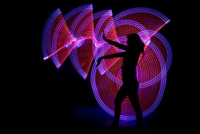 Side view of silhouette woman standing against light painting in darkroom