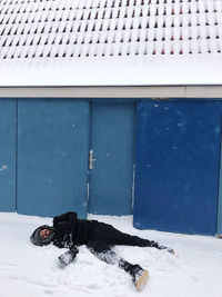 Man in the snow next to a blue building