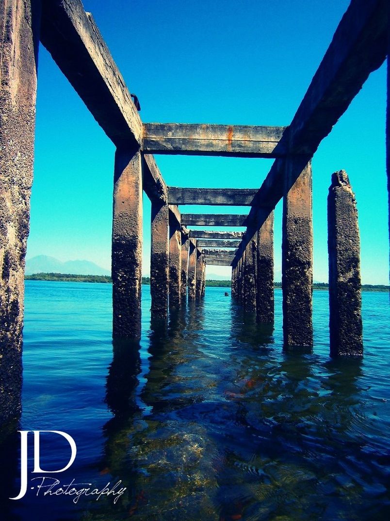 built structure, blue, water, architecture, sea, clear sky, connection, bridge - man made structure, sunlight, architectural column, day, sky, engineering, bridge, diminishing perspective, no people, pier, below, support, nature