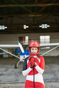 Young female skydiver in a plane hangar with a plane behind her