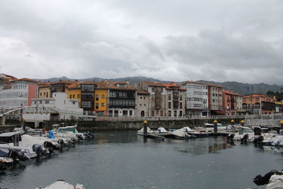 Boats moored at harbor in city against sky