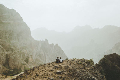 People on rocks by mountains against sky