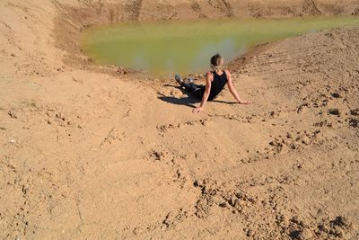 Rear view of woman sitting on sand by water