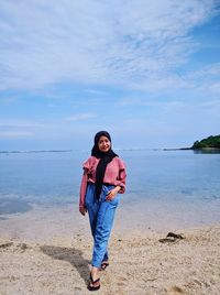 Portrait of young woman standing at beach against sky