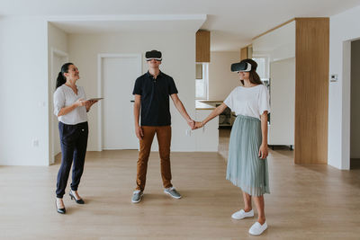 Smiling couple wearing virtual reality simulators while standing by real estate agent on floor