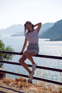 Woman in a white t-shirt and striped shorts and sunglasses sit  fence sea view mountain in marmaris