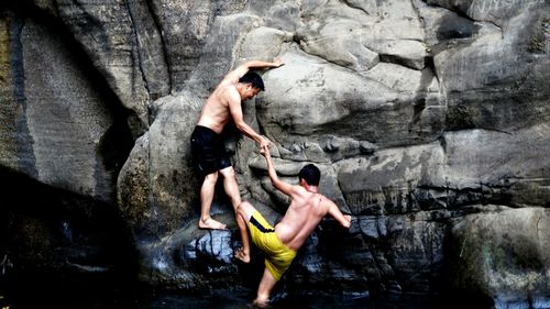 Man assisting friend in climbing on rock