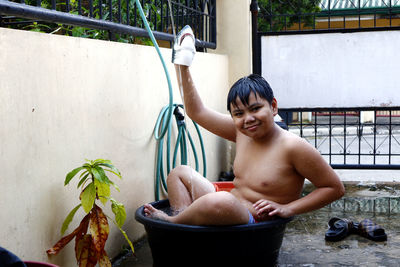 Asian boy cooling down in a water basin and a hose as a makeshift shower to beat the summer heat.