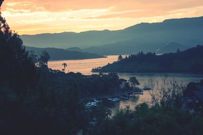 Scenic view of river by silhouette mountains against sky at sunset