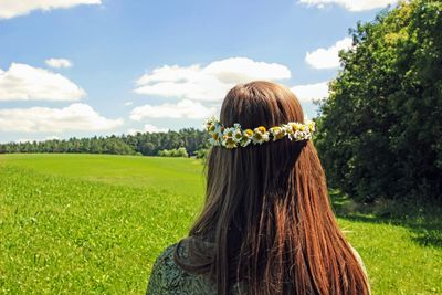 Rear view of woman wearing flowers while standing against sky