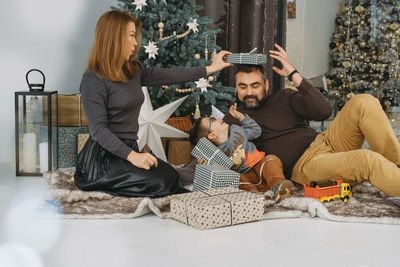 Family with child playing near christmas tree. child unpacking gifts, parents enjoy christmas tree