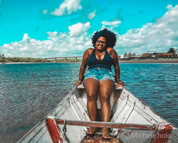 Portrait of smiling young woman sitting on sea against sky