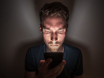 Young man using phone while sitting in darkroom