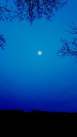 Low angle view of silhouette moon against blue sky at night