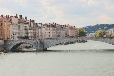 Arch bridge over river by buildings against sky