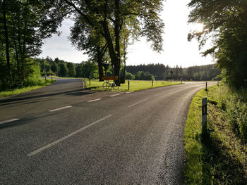 Empty road by trees in city against sky