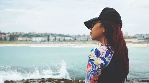 Side view of young woman standing against sea