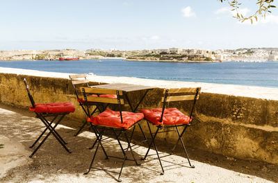 Empty chairs on beach against sky
