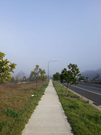 Empty road amidst field against clear sky