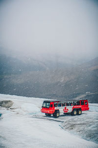 Red car on snow covered land against sky