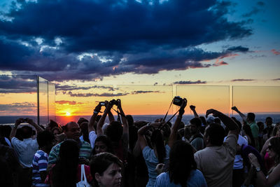 People photographing sea and cloudy sky during sunset