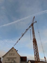 Low angle view of crane by building against sky