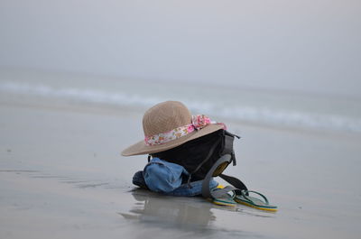 Sun hat over bag by flip-flop at beach