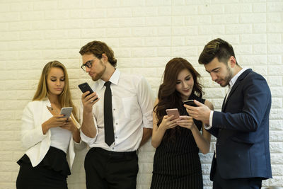 Business colleagues using phones while standing against white brick wall