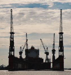 Cranes at commercial dock against sky