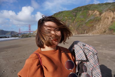 Woman with orange top, brown hair, walking  at baker beach 