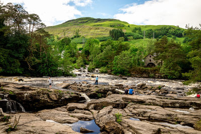 People standing on rock formations by mountains against sky