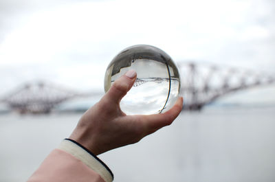 Cropped hand of woman holding crystal ball against bridge in city