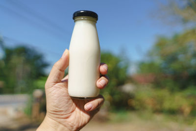 Close-up of hand holding glass bottle against sky