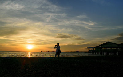 Silhouette of man photographing at beach during sunset