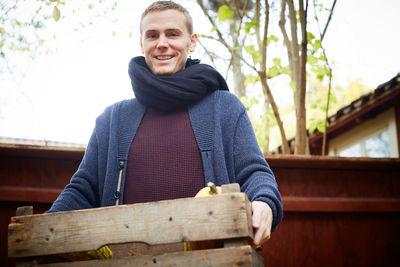 Portrait of happy man standing with vegetable basket in back yard