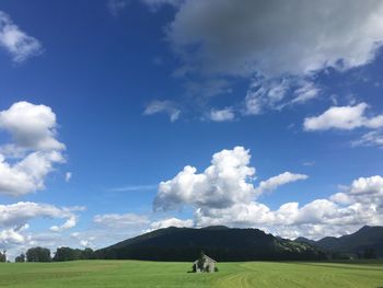 Mid distant house on grassy field by mountain against sky