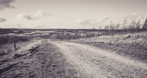 Dirt road amidst field against sky