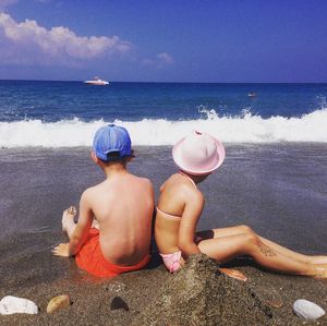 Boy and girl siting on beach against sky