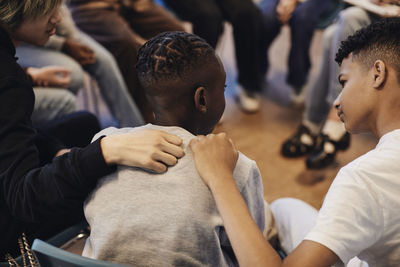 Multiracial boys consoling male friend with arms around in group therapy at school
