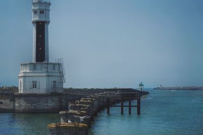 Lighthouse by sea against clear sky