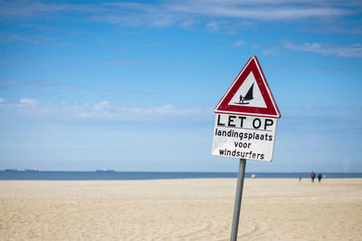 Curious information sign on beach against sky