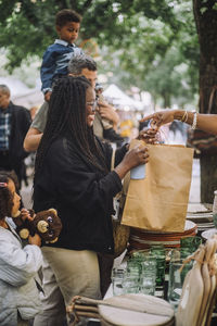 Smiling woman holding paper bag while doing shopping with family at flea market