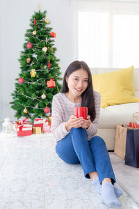 Young woman sitting on christmas tree at home