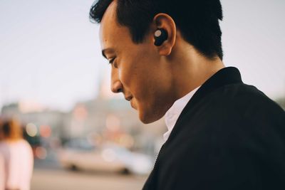 Side view of smiling man wearing in-ear headphones in city