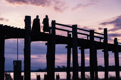 Silhouette people standing by railing against sky during sunset