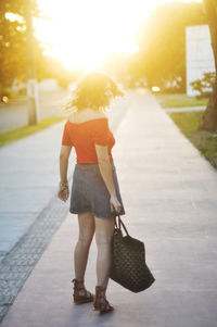 Rear view of woman standing on street in city during sunset