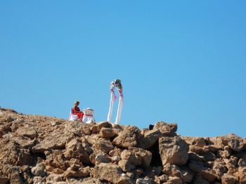 Low angle view of woman sitting on rock against clear blue sky